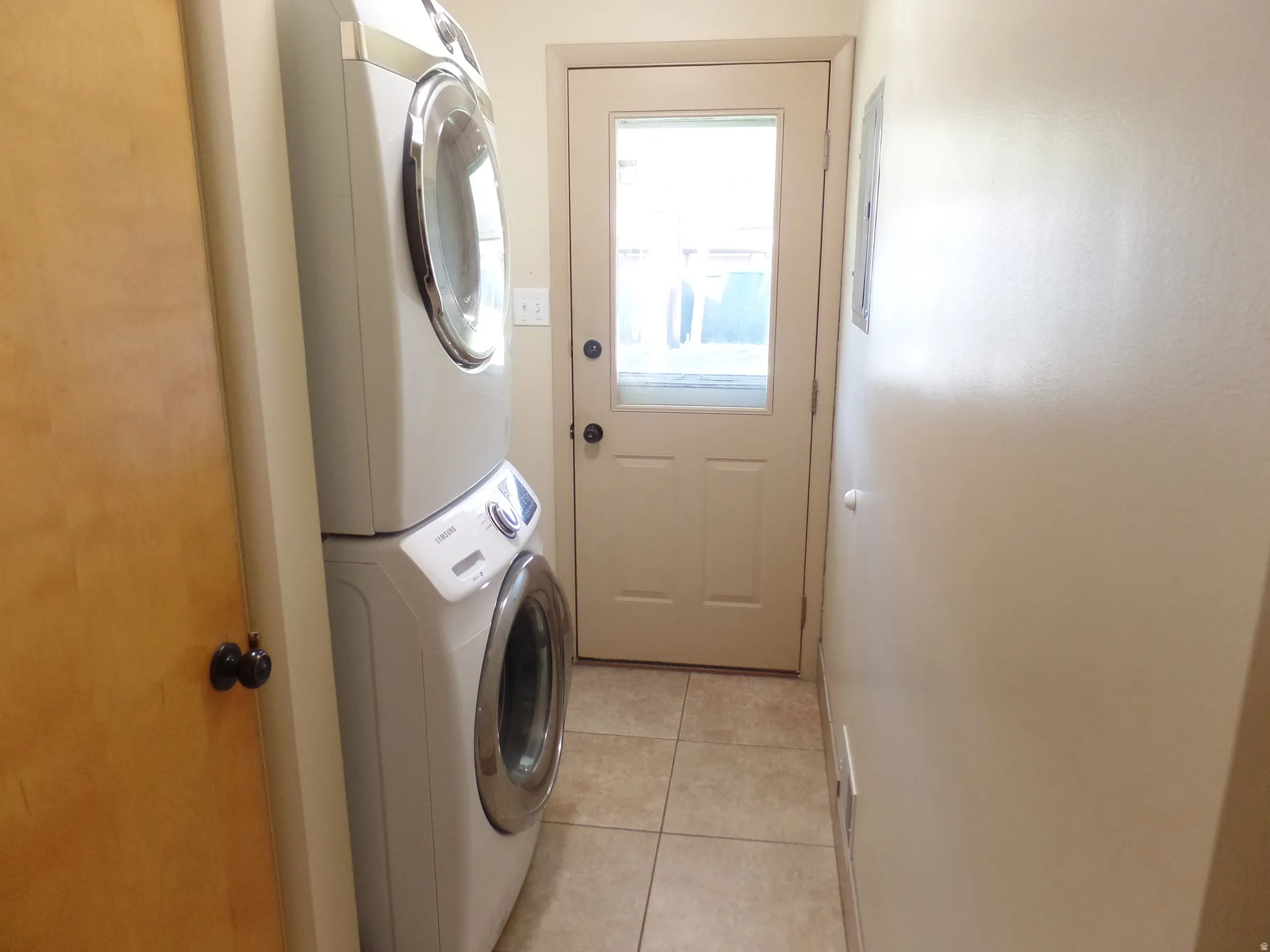 Laundry area featuring stacked washer / dryer, light tile patterned flooring, and electric panel