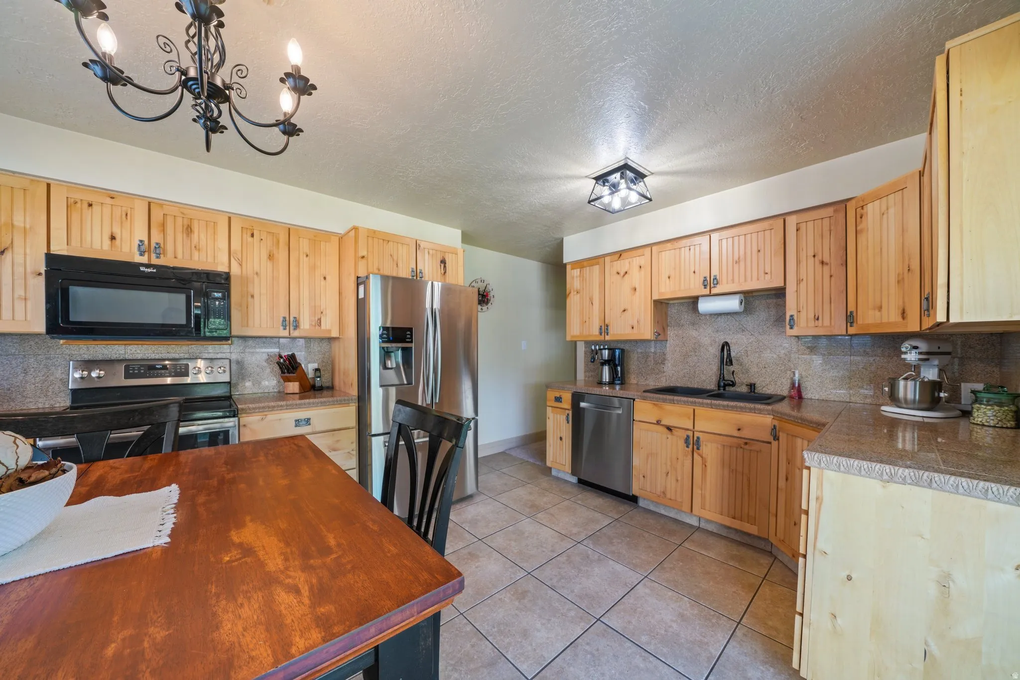 Kitchen with light wood finish cabinetry, stainless steel appliances, light tile patterned floors, decorative backsplash, and a textured ceiling