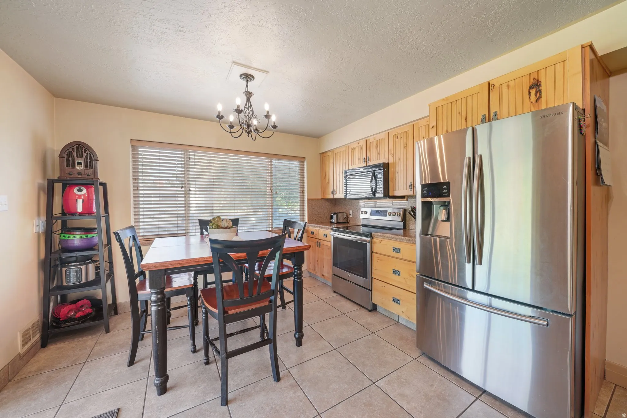 Kitchen with stainless steel appliances, light wood finish cabinetry, suspended lighting, a textured ceiling, and light tile patterned floors