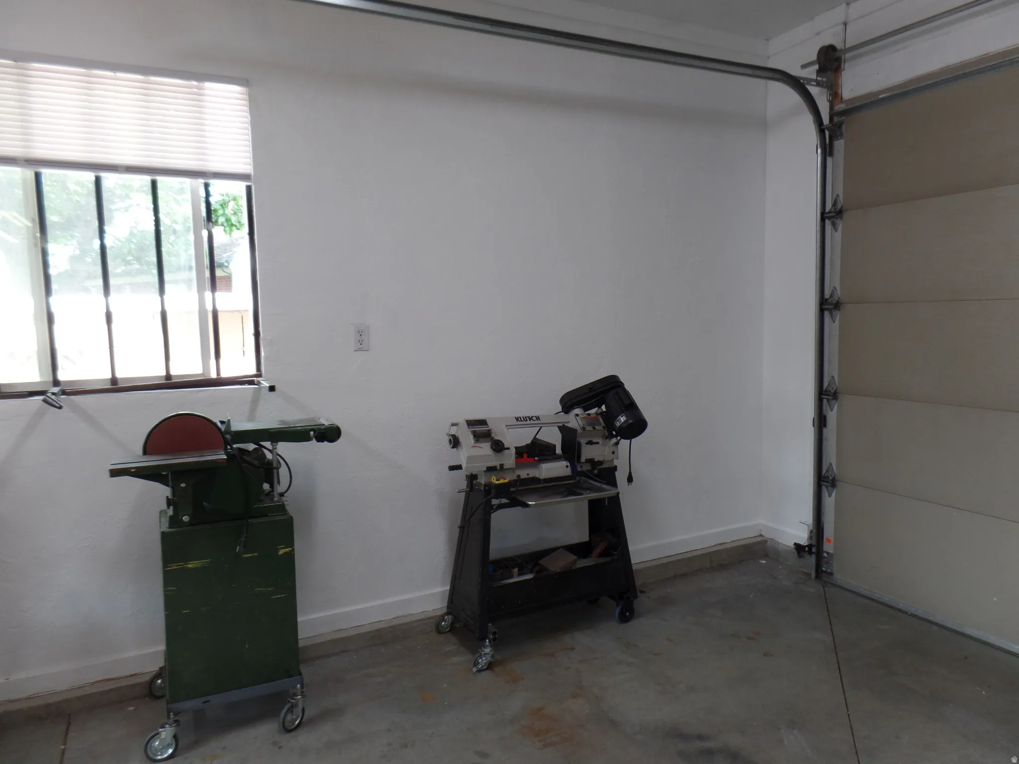 Concrete floor garage space with a window featuring horizontal blinds and security bars