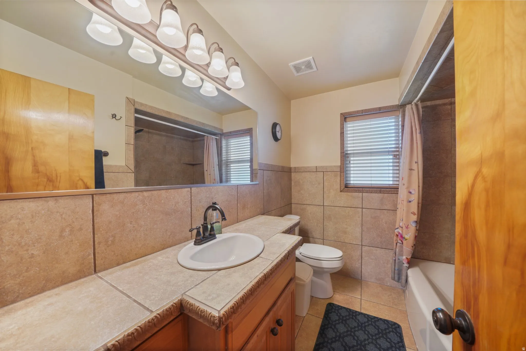 Bathroom with plenty of natural light, vanity, light tile patterned floors, tile walls, and shower / bath combo with shower curtain