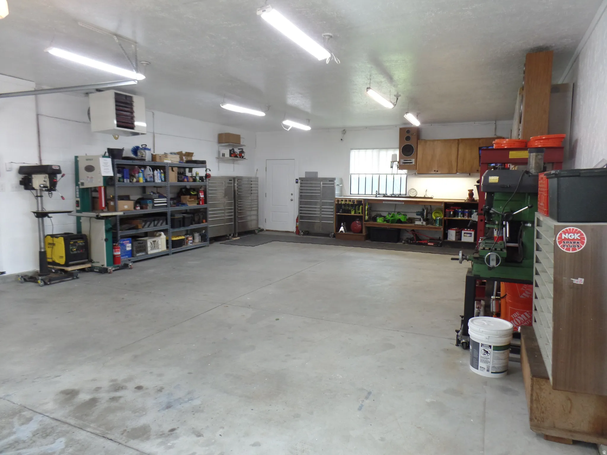 LARGE Garage featuring a workshop area, a heating unit, a 220V outlet, plumbed for air, and cabinets Spacious concrete-floored garage featuring multiple LED light fixtures, a wall-mounted heater, and extensive built-in shelving and cabinetry