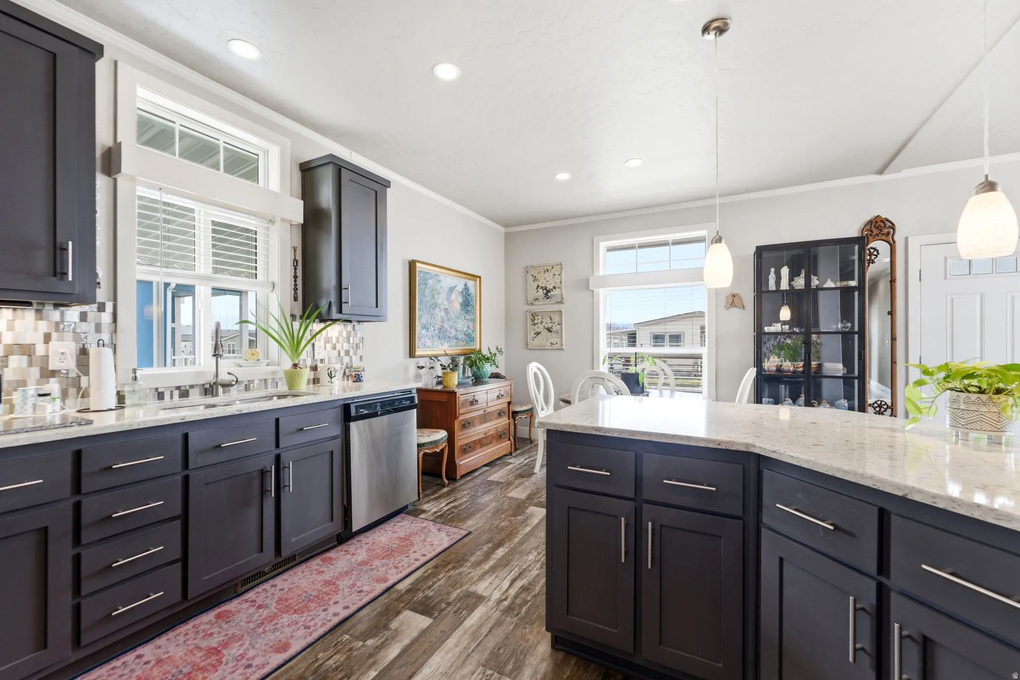 Kitchen with light stone countertops, decorative backsplash, stainless steel dishwasher, dark wood finished floors, and crown molding