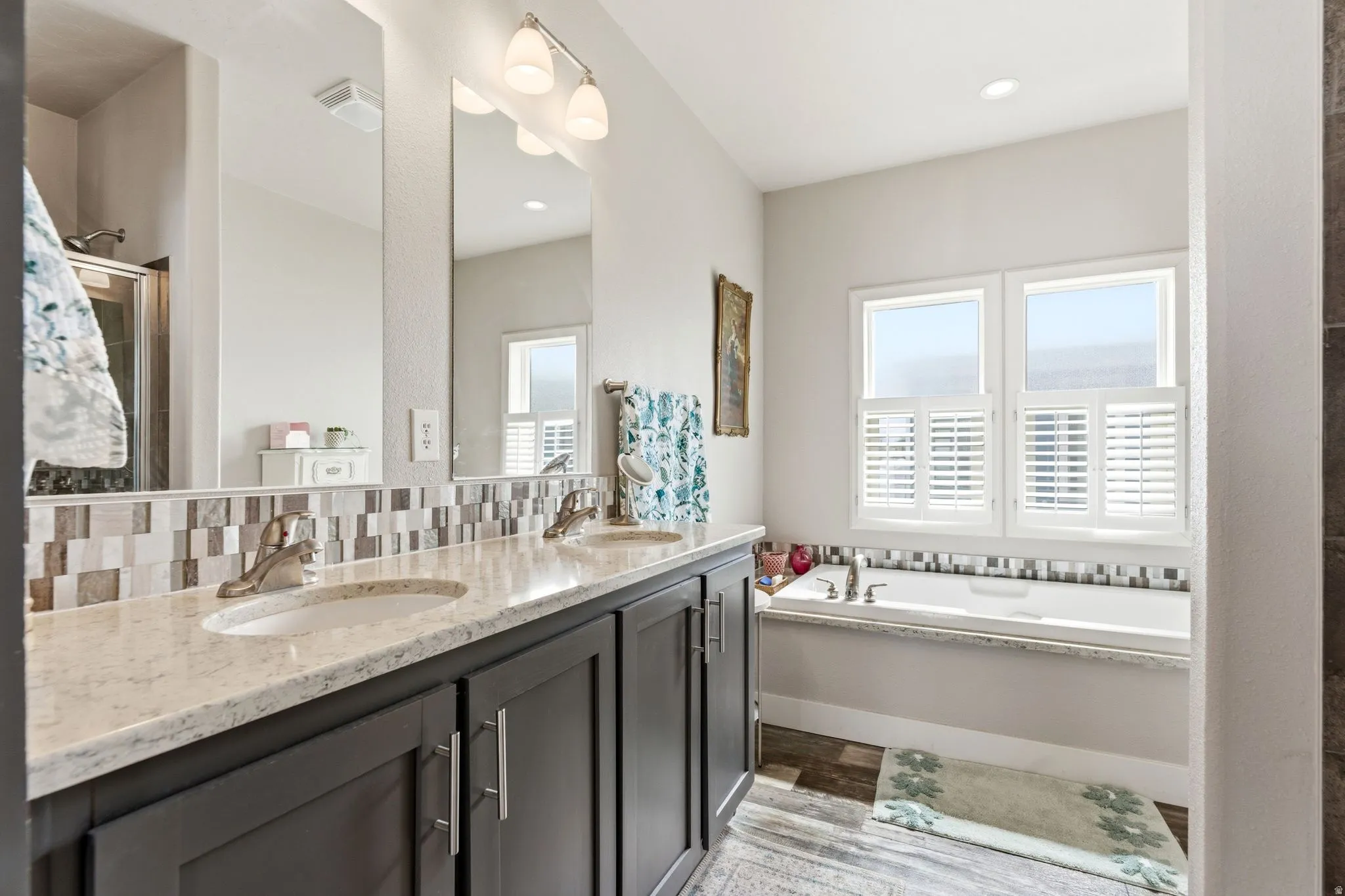 Bathroom featuring double vanity, a stall shower, a bath, light wood-style floors, and decorative backsplash