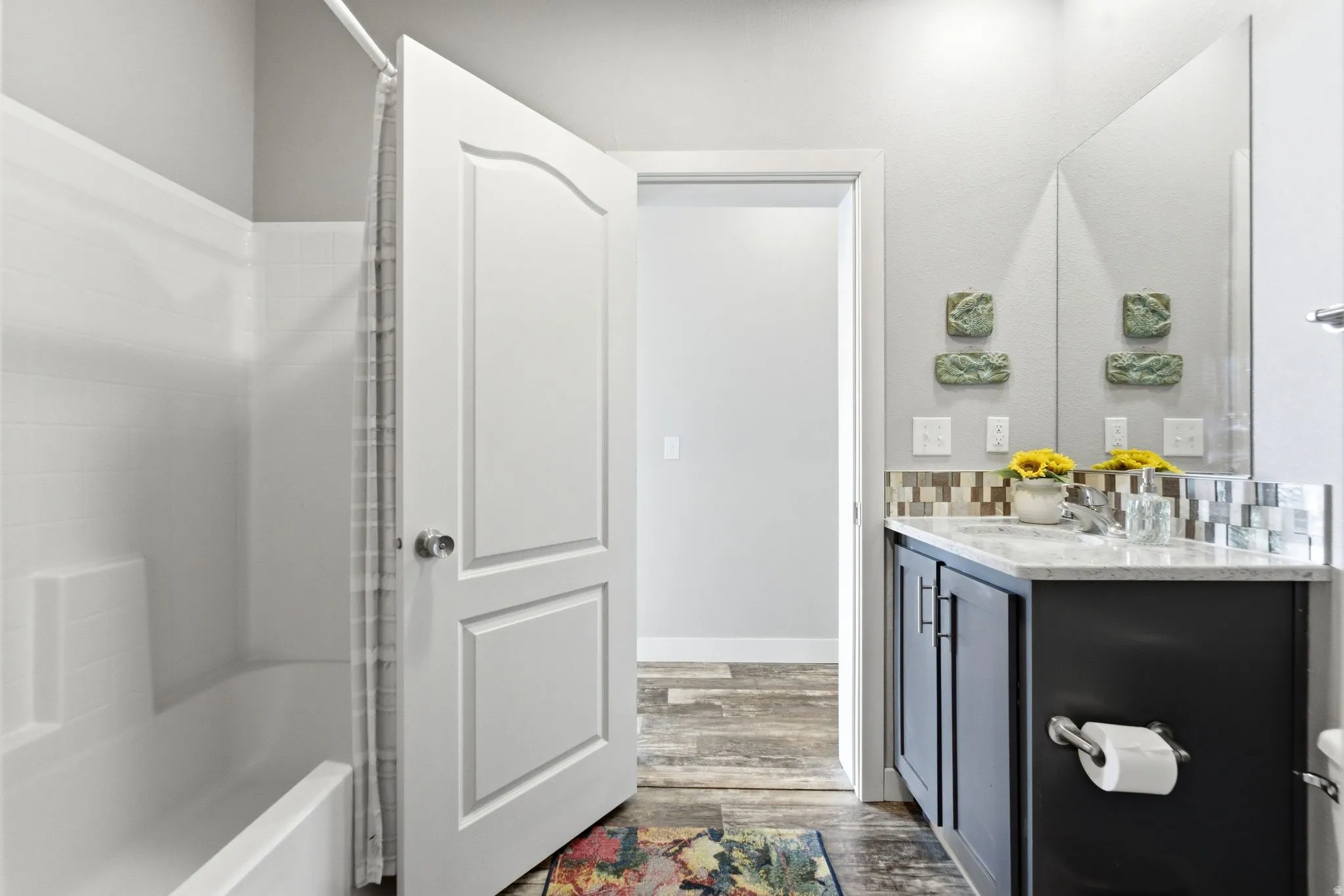 Bathroom with vanity, dark wood-style flooring, bathing tub / shower combination, and decorative backsplash