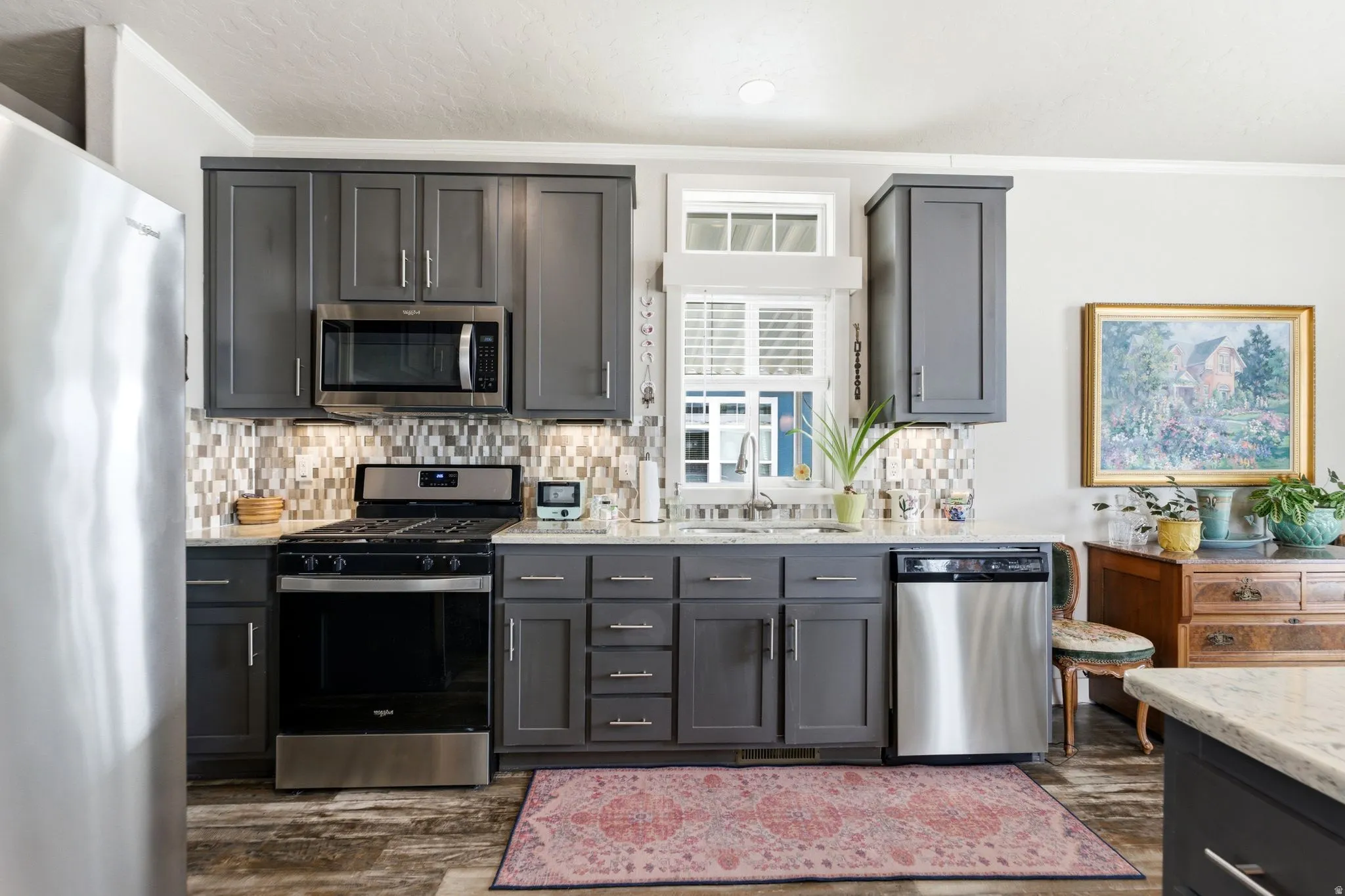 Kitchen featuring stainless steel appliances, ornamental molding, light stone countertops, backsplash, and dark wood-style flooring