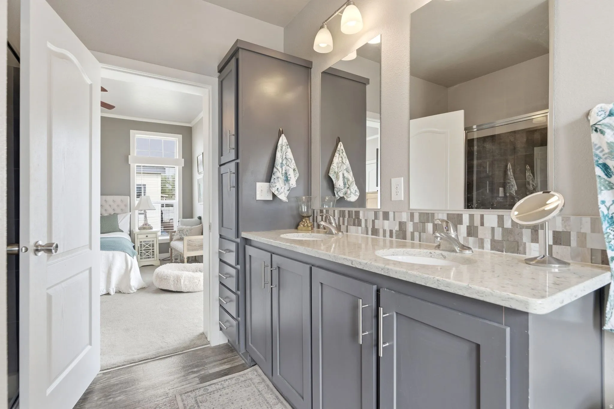 Ensuite bathroom with double vanity, tasteful backsplash, light wood-style floors, and crown molding