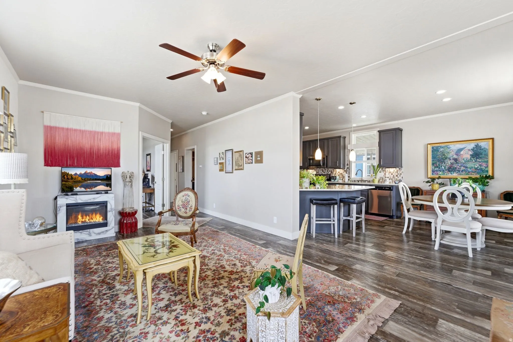 Living room featuring ceiling fan, a glass covered fireplace, ornamental molding, and dark wood-style flooring