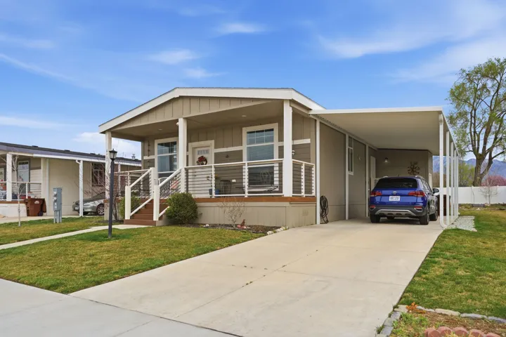 Manufactured / mobile home with a front lawn, covered porch, a carport, concrete driveway, and board and batten siding