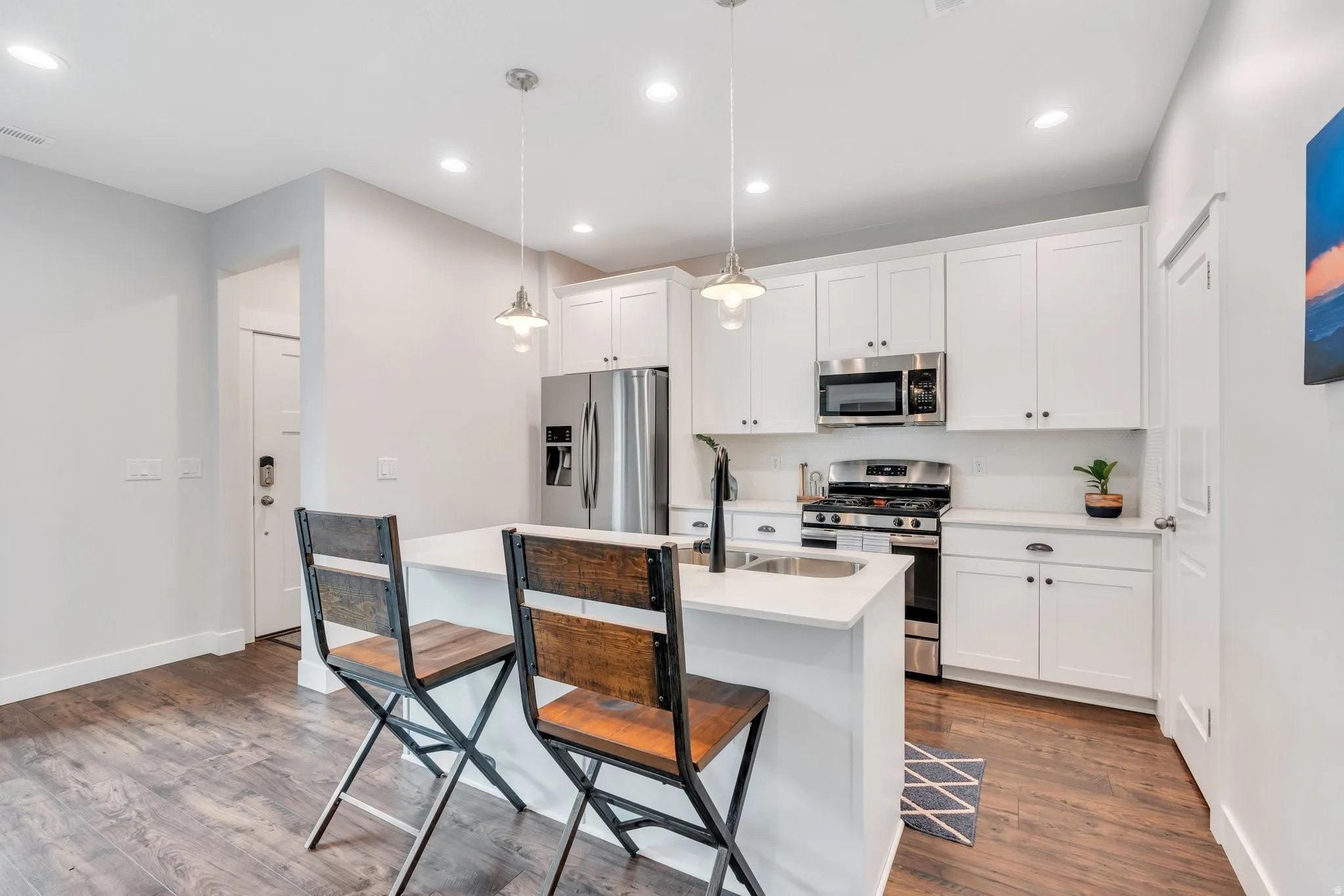 Kitchen with stainless steel appliances, white cabinetry, a breakfast bar, a center island with sink, and dark wood-type flooring