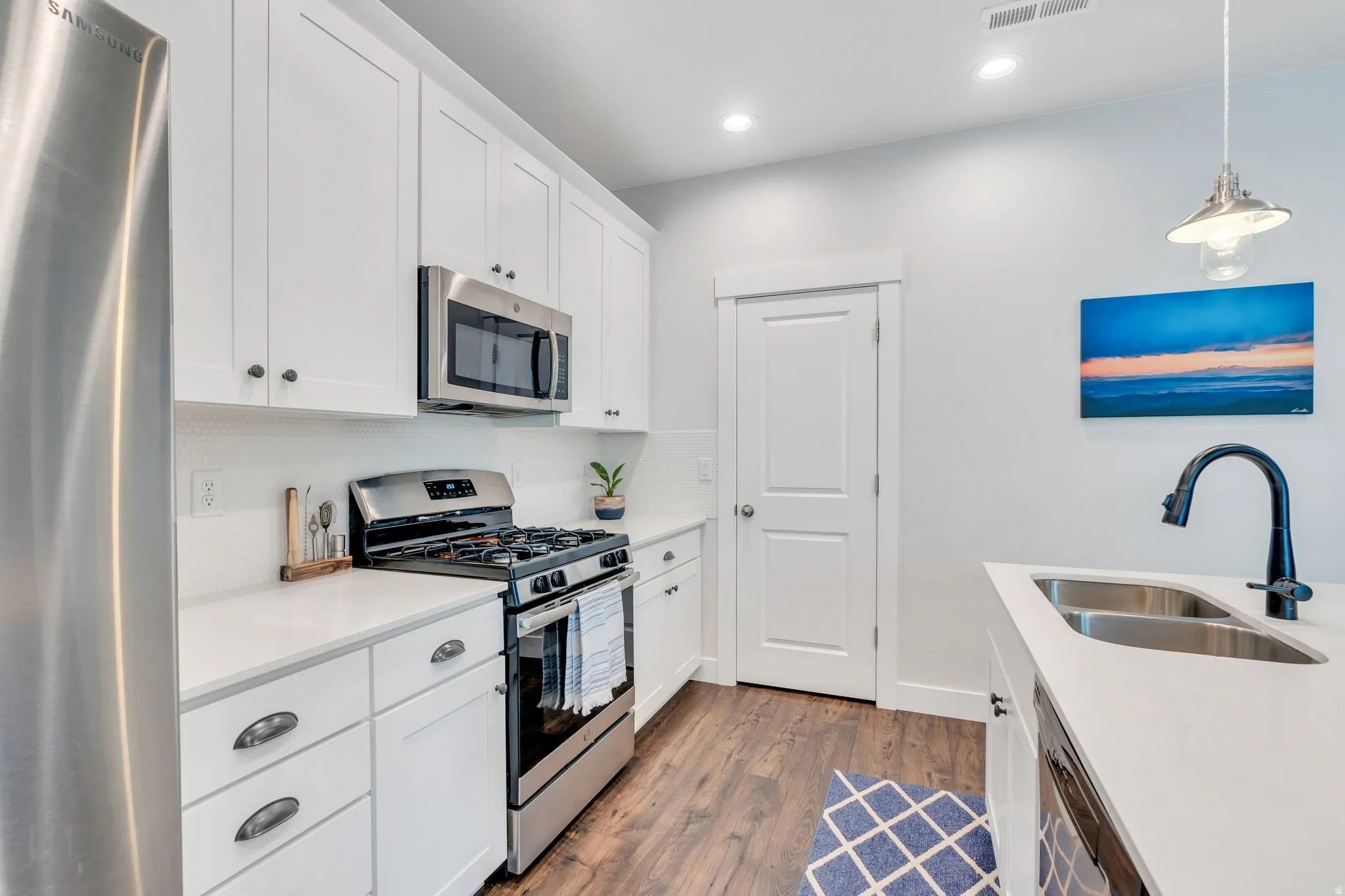 Kitchen with stainless steel appliances, white cabinets, dark wood finished floors, pendant lighting, and light stone countertops