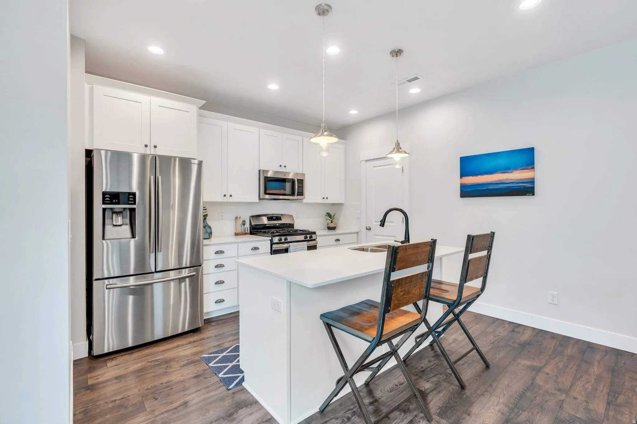 Kitchen featuring crisp cabinetry with elegant crown molding, a large island with built-in sink, SS appliances and chic lighting!