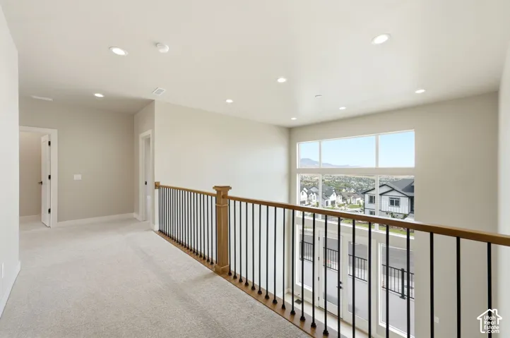 Expansive second-floor landing featuring recessed ceiling lighting, wood-finish railings with metal balusters, and abundant natural light from large windows overlooking the surrounding neighborhood
