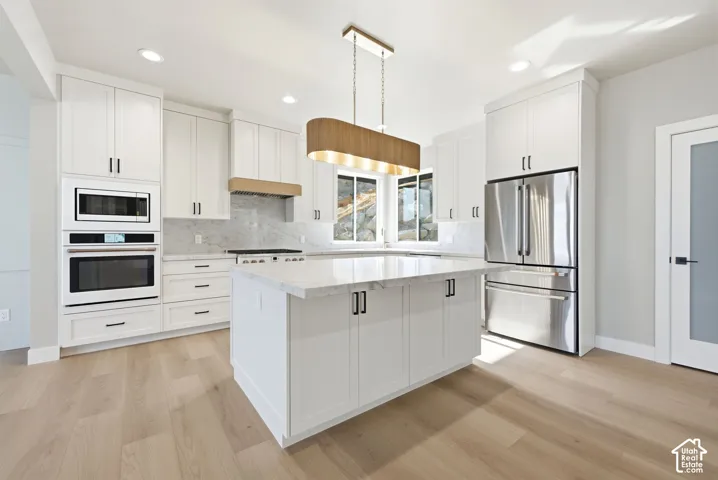 Kitchen featuring a central island with countertop, white cabinetry with black hardware, stainless steel appliances, and wood-finish flooring. Refrigerator included.
