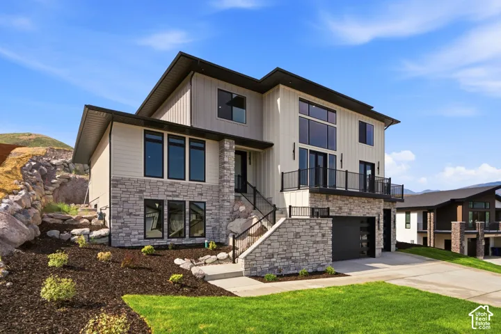 Contemporary exterior featuring vertical siding, stone accents, black-framed windows, a black garage door, and a second-story balcony with metal railings