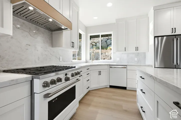 White cabinetry, light wood-finish flooring, stainless steel appliances, stone slab countertops, and a matching full-height backsplash with cafe appliances.