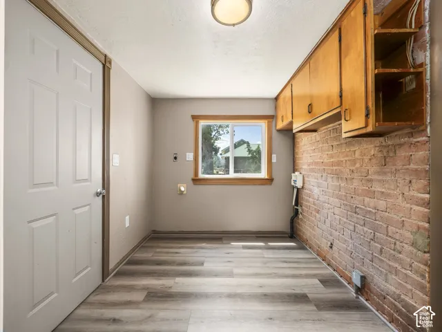 Utility space featuring a brick accent wall, wood-finish flooring, and natural wood cabinetry