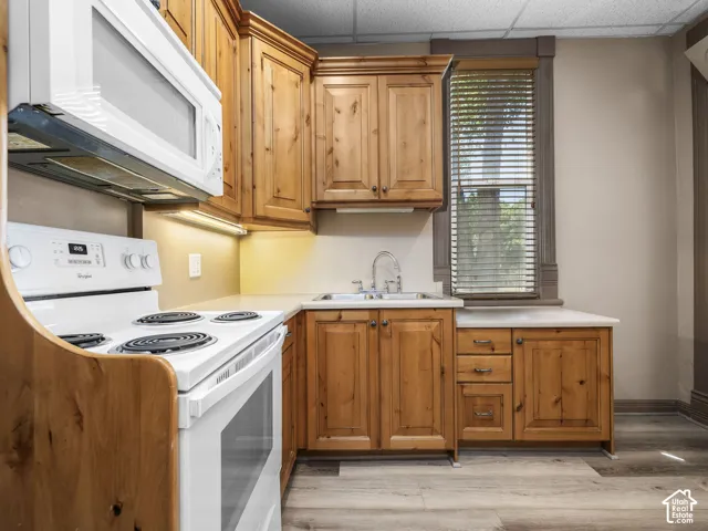 Kitchen featuring wood cabinetry, white appliances, solid surface countertops, and wood-finish flooring