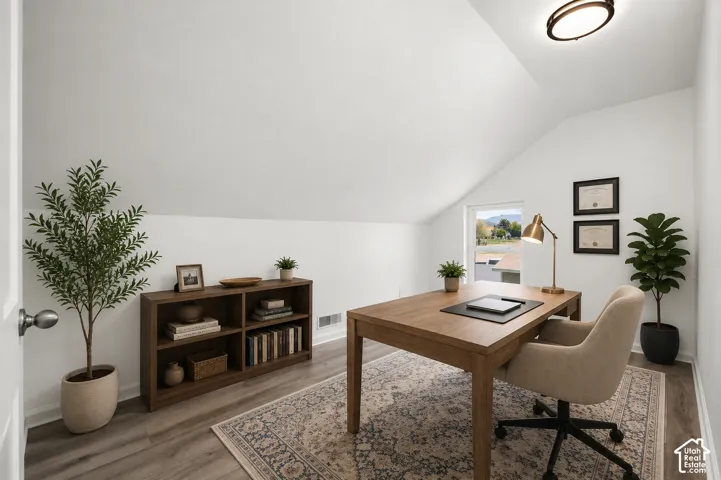 Office space featuring sloped ceilings, a window with distant mountain scenery, wood-finish flooring, and built-in shelving
