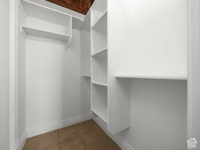 Walk-in closet featuring built-in shelving, hanging rods, baseboard molding, and tile flooring