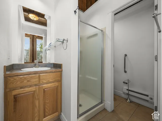Bathroom featuring a wood vanity with a drop-in sink, glass shower enclosure, and tiled flooring