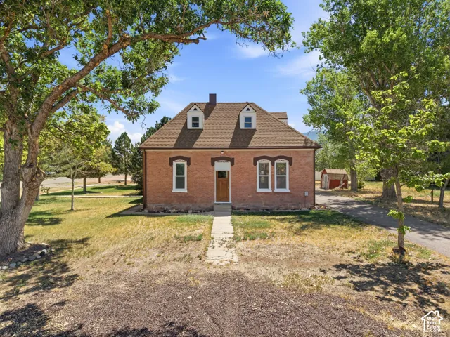 Brick-clad residence featuring a dormer roofline with two gabled dormers, a central wooden entry door, and multiple white-framed windows