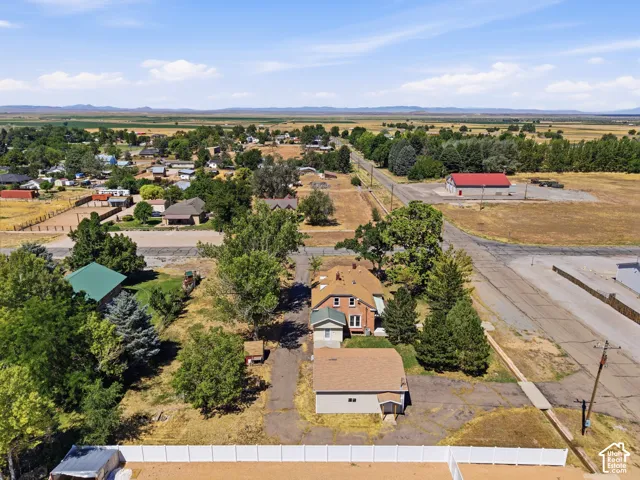 Aerial perspective showcasing a multi-story residence with a red brick exterior, a light-colored detached structure, mature trees, and an open lot
