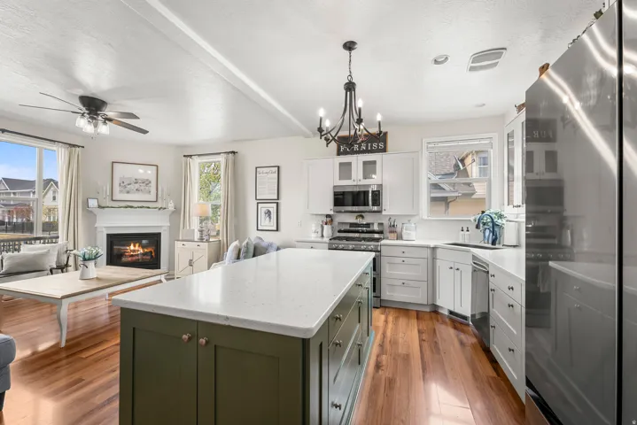 Dual tone kitchen with stainless steel appliances, dual tone cabinetry, glass insert cabinets, light stone counters, and a ceiling fan