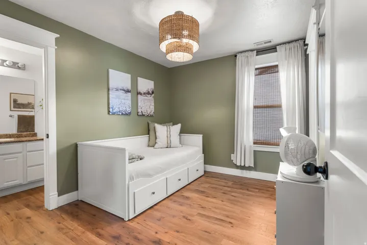Bedroom featuring light wood-type flooring, suspended lighting, and ensuite bath