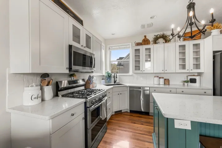 Kitchen with glass fronted cabinets, stainless steel appliances, light stone countertops, dark wood-style floors, and two tone cabinetry
