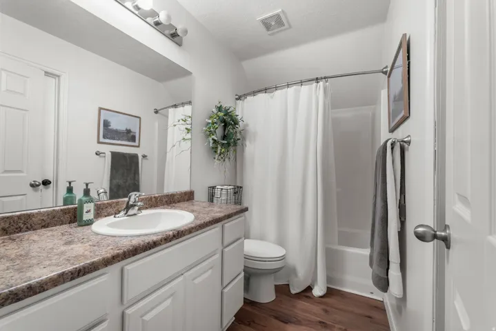 Full bath featuring vanity, dark wood-type flooring, shower / bath combo with shower curtain, and a textured ceiling