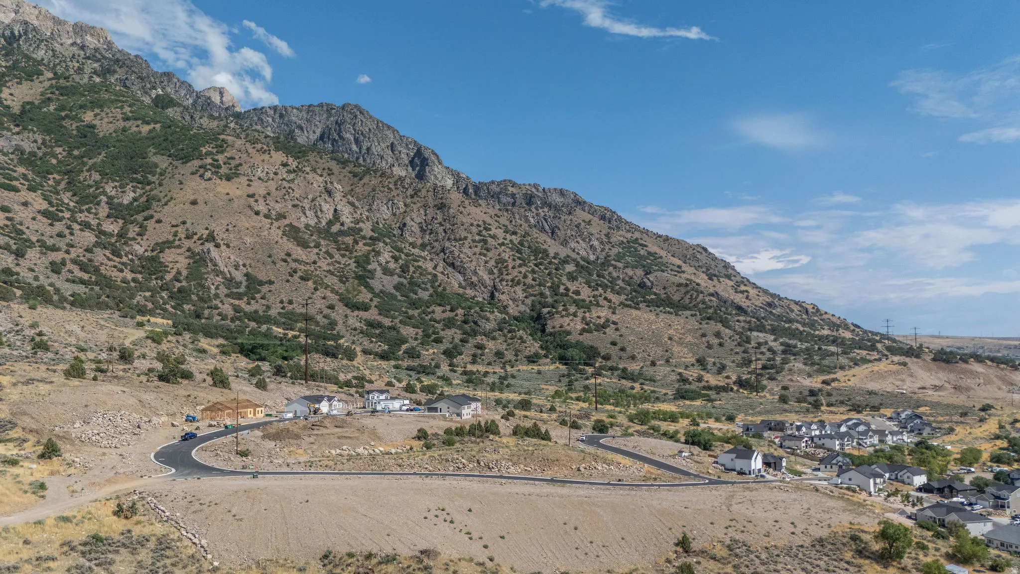 Expansive mountain landscape featuring a development of single-family homes, partially paved roads, and natural terrain