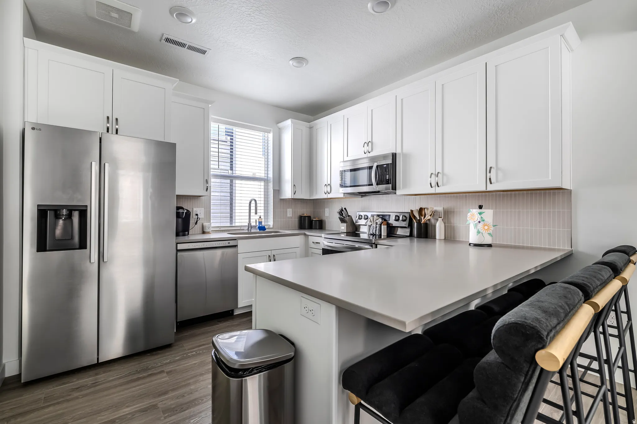 Kitchen with stainless steel appliances, a peninsula, a breakfast bar, white cabinets, and light countertops