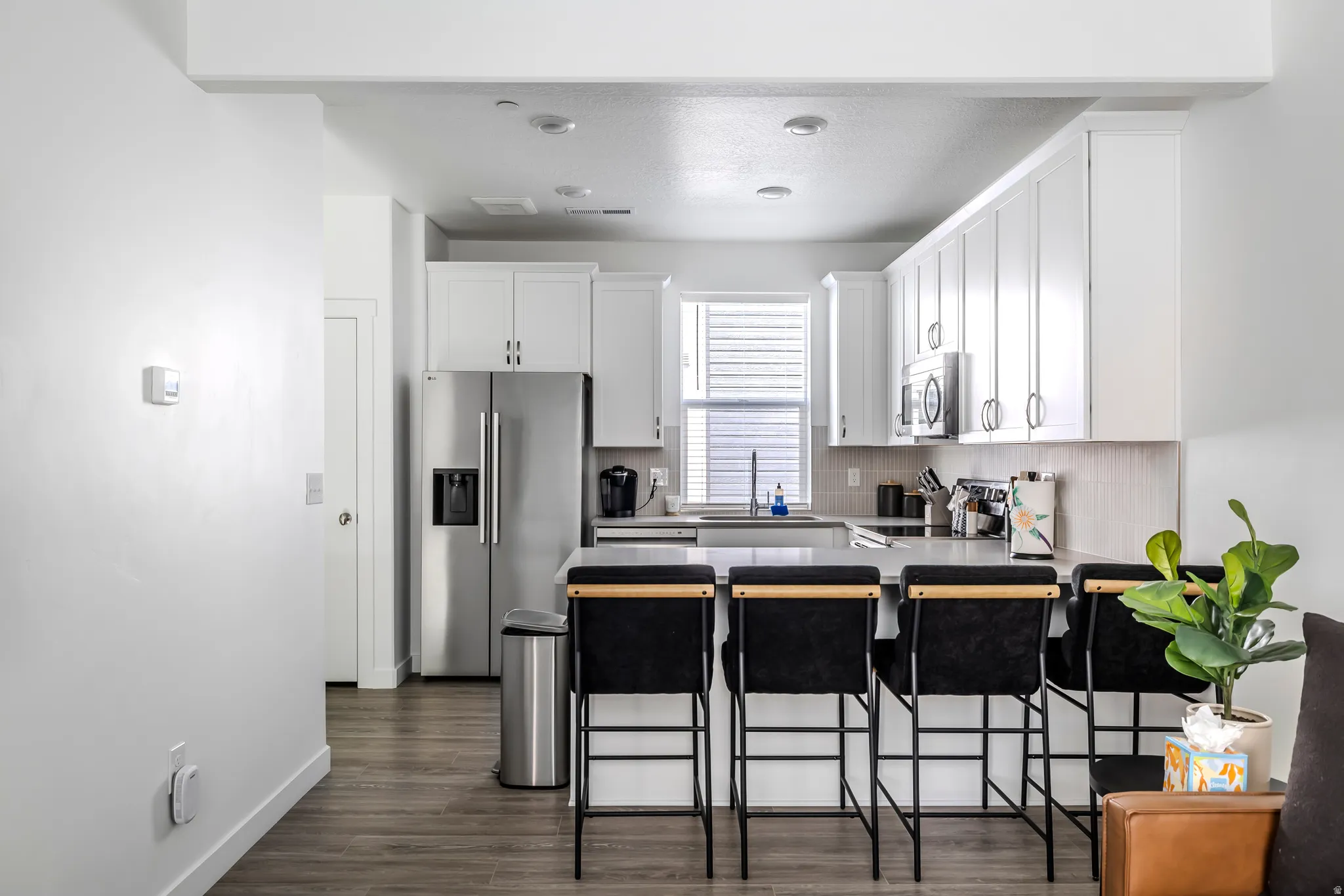 Kitchen with a peninsula, a breakfast bar area, stainless steel appliances, white cabinetry, and dark wood-style flooring