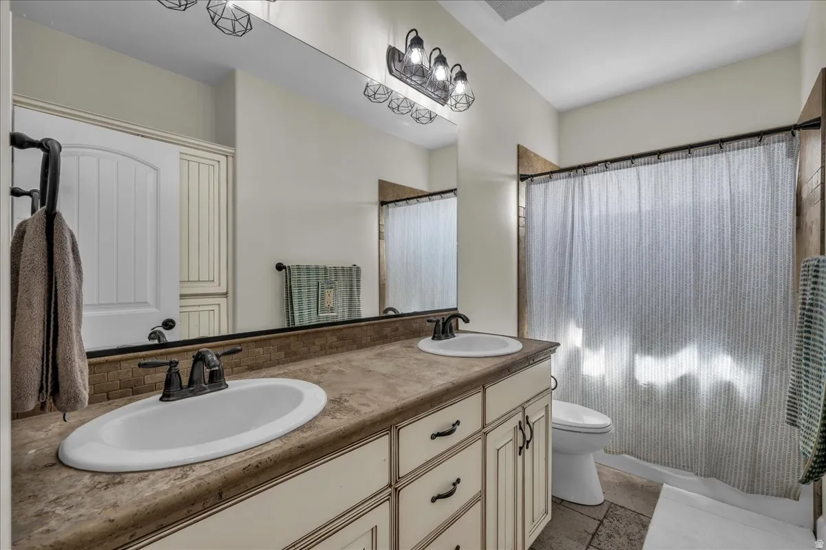 Bathroom with double vanity, stone tile flooring, and a shower with curtain