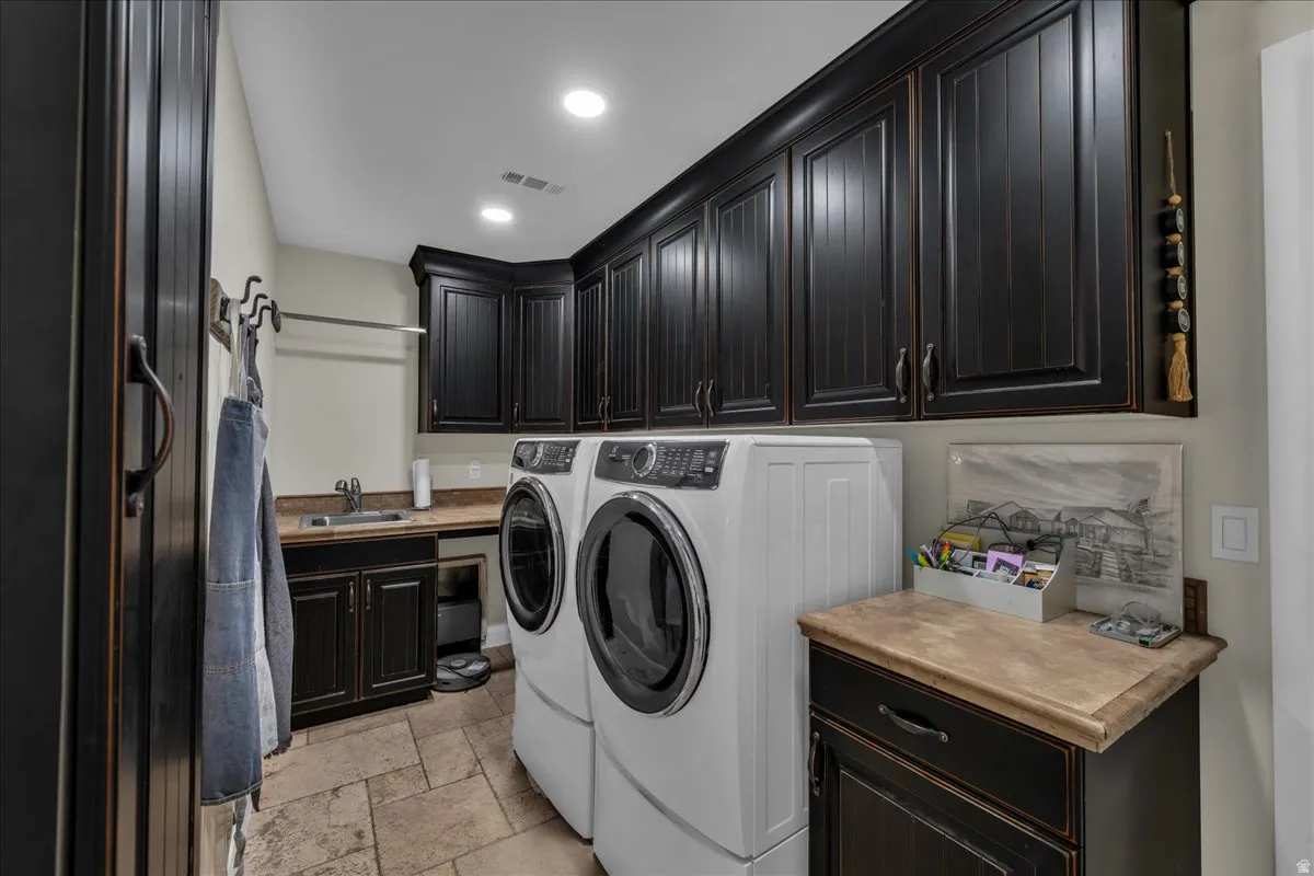 Laundry room with stone tile flooring, washer and clothes dryer, cabinet space, and recessed lighting