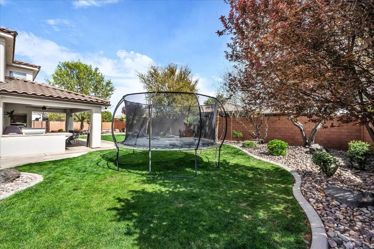 Fenced backyard featuring a trampoline, a patio area, an outdoor kitchen, and a ceiling fan