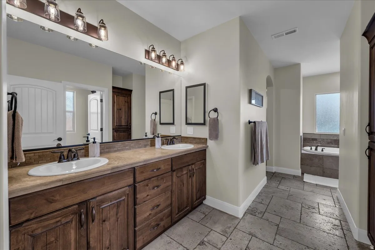 Bathroom with double vanity, stone tile flooring, a garden tub, and plenty of natural light