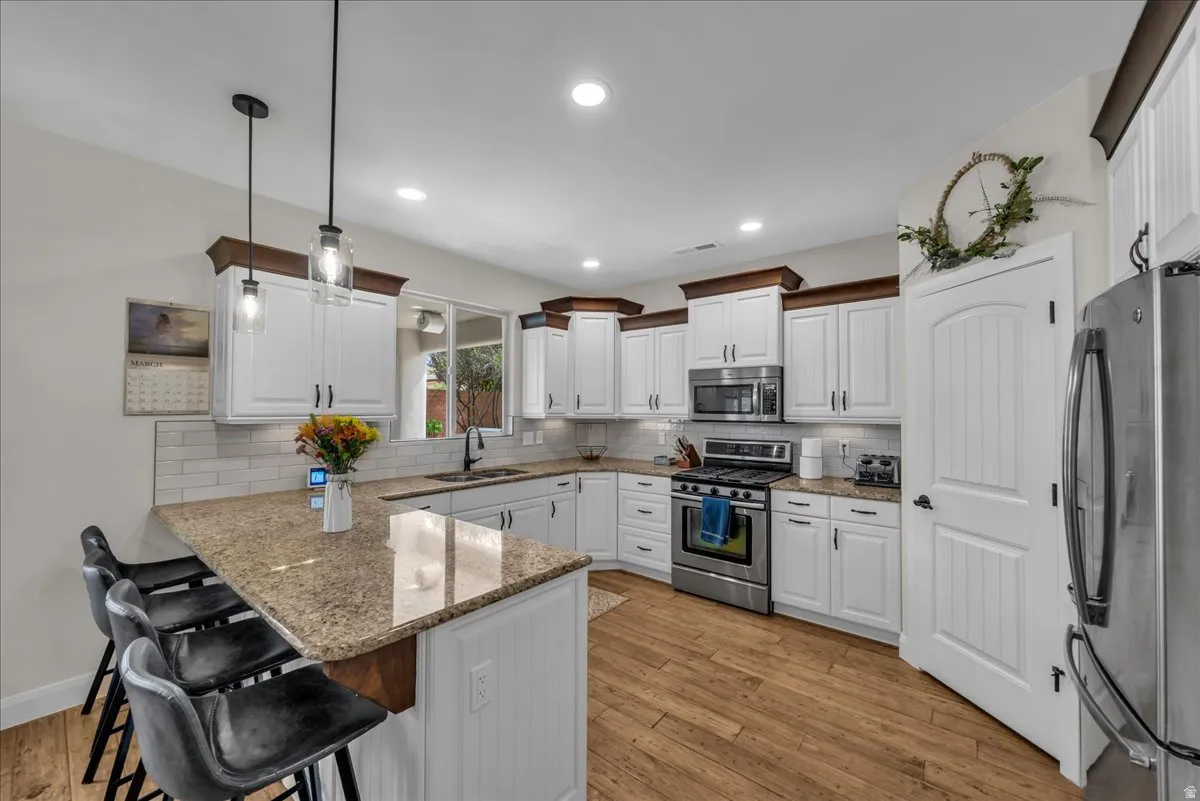 Kitchen with a peninsula, stainless steel appliances, a breakfast bar, light wood finished floors, and light stone counters