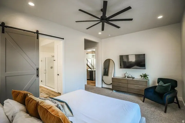 Bedroom with a barn door, ensuite bath, ceiling fan, light carpet, and recessed lighting