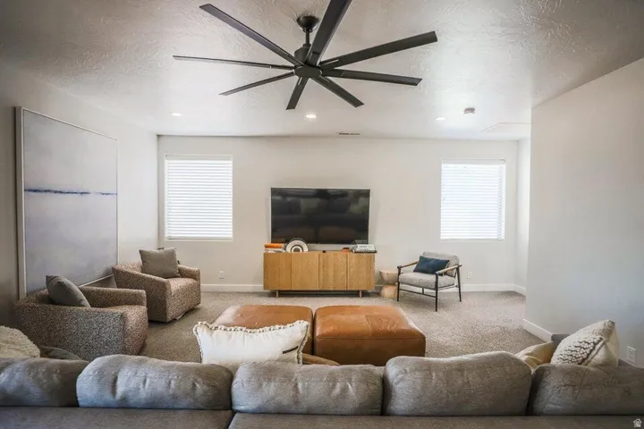 Carpeted living room with a textured ceiling, ceiling fan, and healthy amount of natural light