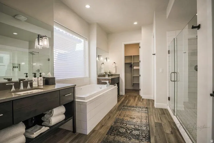 Full bathroom featuring a bath, a stall shower, two vanities, dark wood finished floors, and a walk in closet