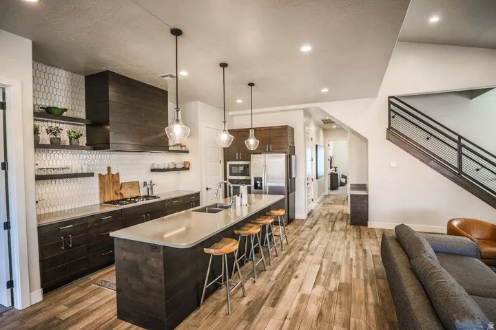 Kitchen featuring dark wood finish cabinets, open shelves, an island with sink, hanging light fixtures, and a kitchen breakfast bar