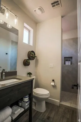 Bathroom featuring tiled shower, vanity, and dark wood finished floors