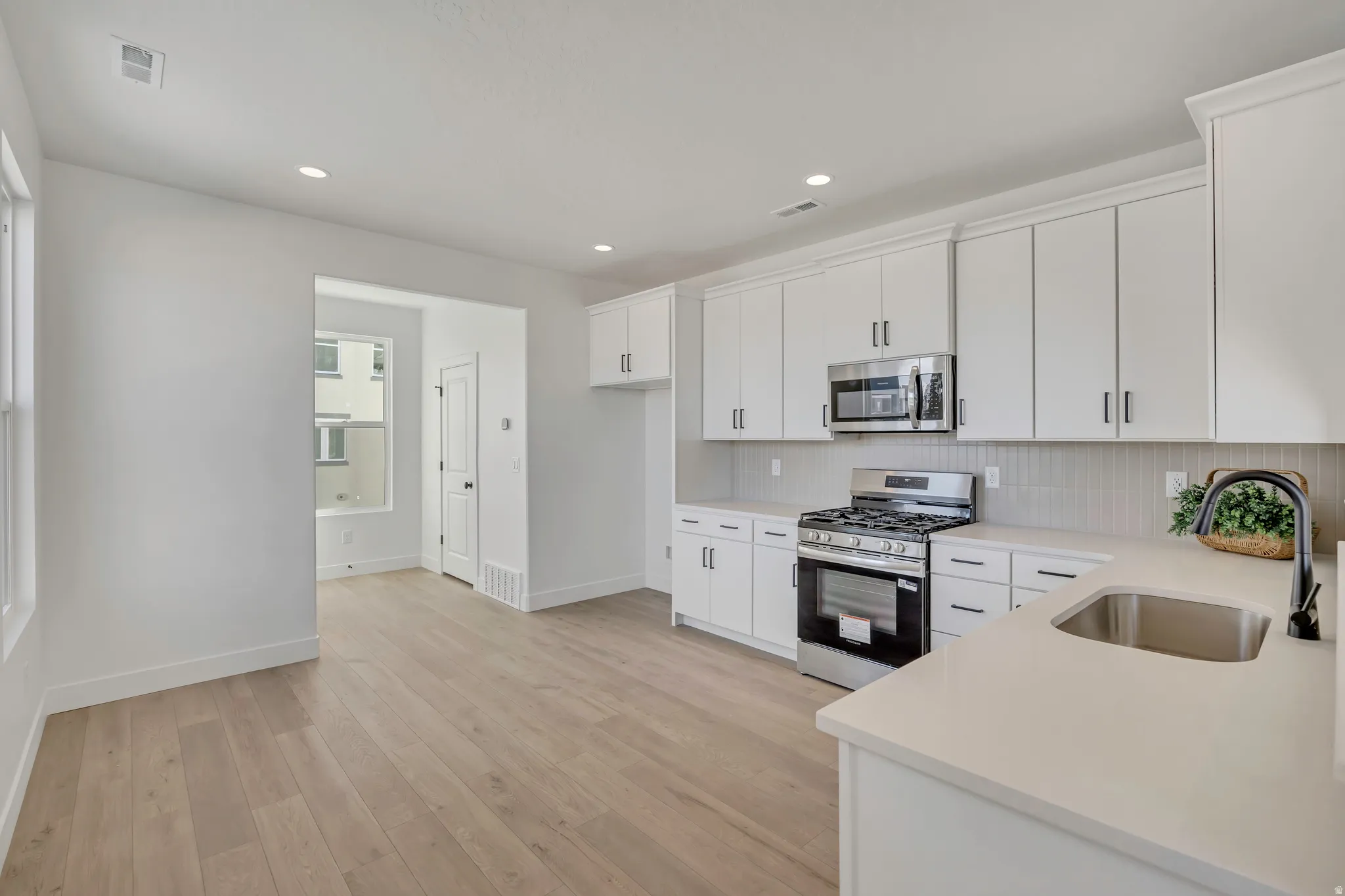 Kitchen with stainless steel appliances, white cabinets, light wood-type flooring, recessed lighting, and tasteful backsplash