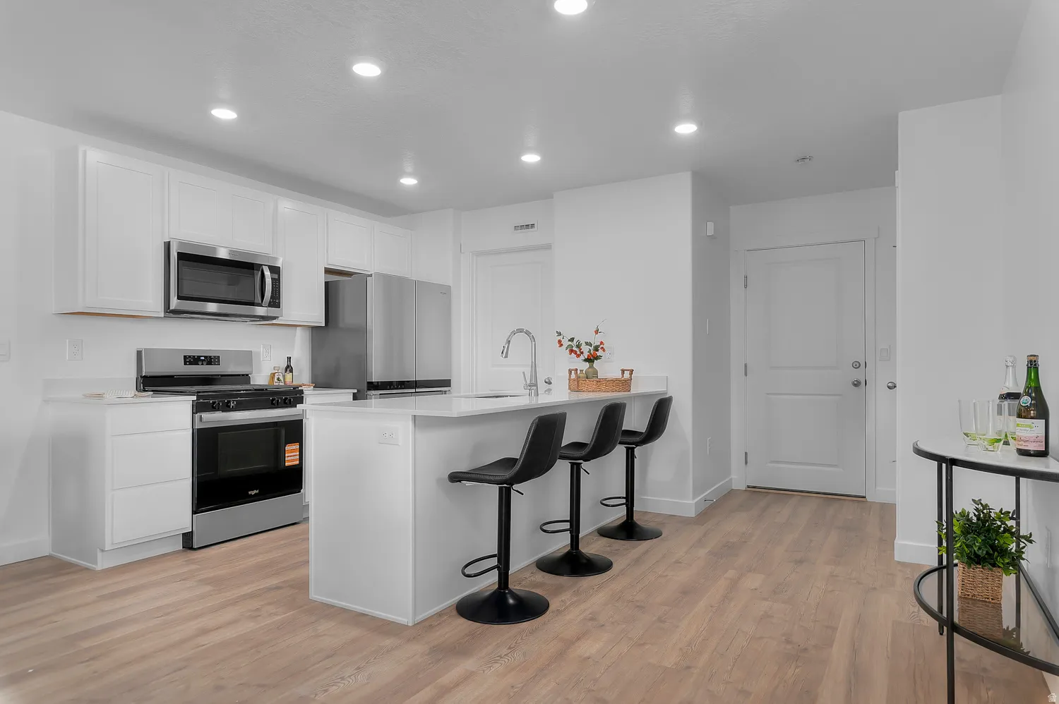 Kitchen featuring a kitchen bar, stainless steel appliances, white cabinets, light wood finished floors, and recessed lighting