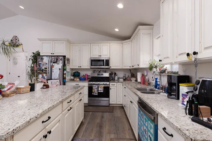 Kitchen with stainless steel appliances, lofted ceiling, dark wood-type flooring, light stone countertops, and white cabinets