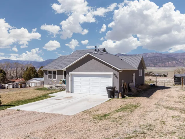 View of side of property featuring a mountain view, driveway, an attached garage, stucco siding, and a metal roof