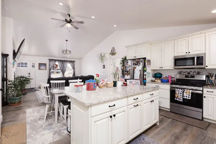 Kitchen with stainless steel appliances, a kitchen island, light stone countertops, open floor plan, and recessed lighting
