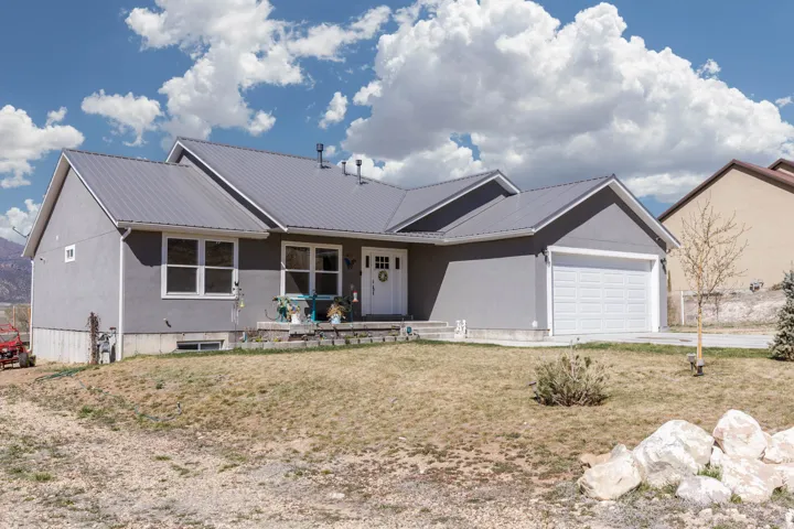 Ranch-style house featuring a metal roof, a garage, a front yard, stucco siding, and concrete driveway